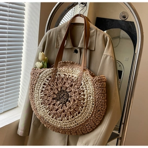 Detail of round straw tote bag featuring brown leather shoulder strap and woven texture