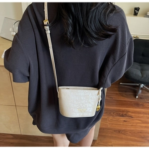 Detail of cream crossbody bag featuring faux crocodile texture and gold heart charm