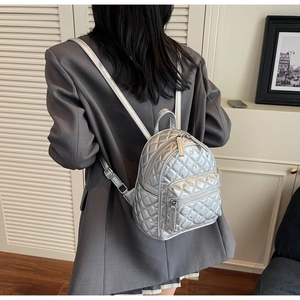 Detail of silver quilted mini backpack with metallic finish on model in modern interior