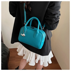 Detail of lake blue pebbled leather handbag featuring silver whale charm and dual handles