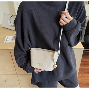 Detail of white crocodile pattern crossbody bag with a golden heart pendant and logo