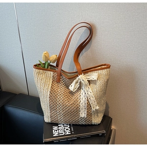 Détail d'un sac cabas en paille tressée avec anses en cuir marron et nœud en dentelle