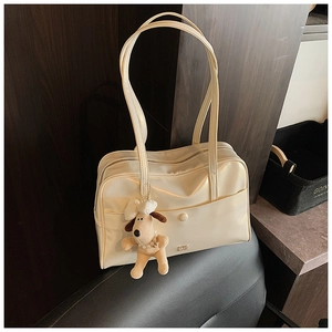Detail of cream white leather shoulder bag featuring a cute plush dog pendant and gold logo