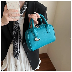 Detail of teal leather bowling bag with silver whale charm and pebble texture finish