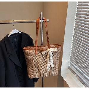 Détail du sac cabas en paille tressée avec bandoulières en cuir marun et nœud en dentelle