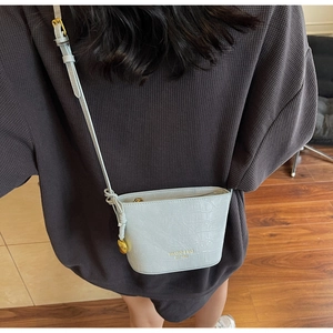 Detail shot of light gray faux crocodile bucket bag with adjustable gold charm strap