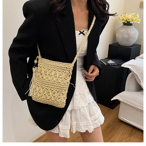 Detail of hand-woven straw crossbody bag with floral texture and tassel on black blazer