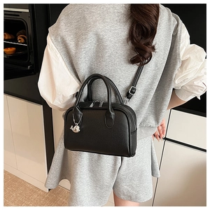 Detailed view of black litchi leather handbag with silver dolphin charm and dual zippers