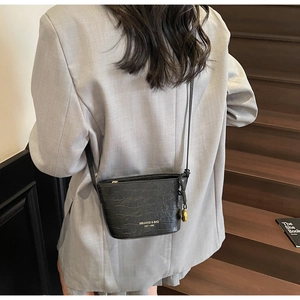 Close-up of black crocodile pattern bucket bag with gold lettering on a wooden staircase