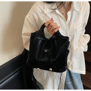 Close-up of black glossy leather bucket bag with bow drawstring and silver metal charms