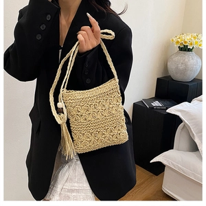 Detail of bohemian straw crossbody bag featuring hollow flower pattern and tassel charm