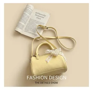 Detail of pale yellow Boston bag featuring pearl heart and lace bow charms on leather