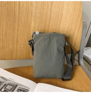 Close-up of a sage green nylon phone bag with drawstring and adjustable strap on a chair