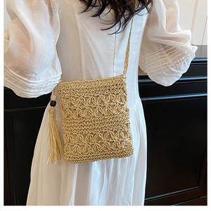 Detail of handmade straw woven crossbody bag featuring hollow flower patterns and tassels