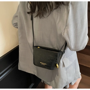 Detail of black crocodile texture crossbody bag with gold text print on gray suit