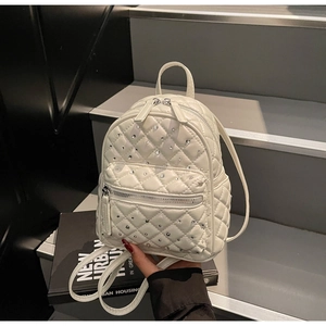 Detail of white quilted mini backpack featuring sparkling rhinestone accents and dual zippers