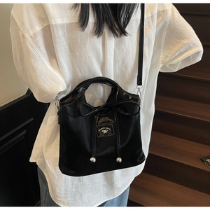 Detail shot of a black patent leather handbag featuring a bow and brand logo patch