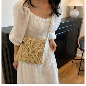 Detail of straw crossbody bag with floral weave and long tassel on white dress