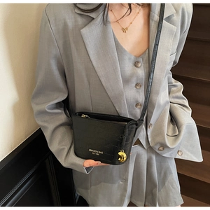 Chic black crocodile pattern crossbody bag styled with a grey suit on a model