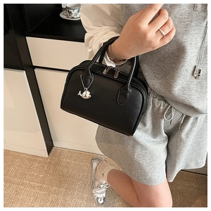 Close-up of black lychee grain leather handbag with silver whale charm and dual zipper detail