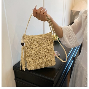 Detail of beige straw bag with hollow flower weave patterns and bohemian fringe tassels