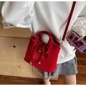 Detail view of a glossy red bucket bag with a bow drawstring and shoulder strap on a model