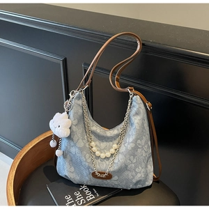 Detail of light blue denim tote bag with brown straps, silver chain and pearl decor