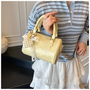 Détail du sac cylindrique jaune clair en cuir plissé brillant avec breloque cœur perle