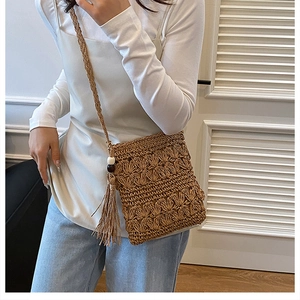 Detail of handmade khaki woven straw bag with boho tassels and decorative wooden beads