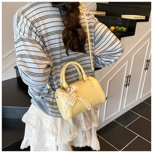 Détail du sac boston jaune avec nœud en dentelle, pendentif cœur perlé et cuir brillant