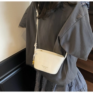 Detail of white bucket bag with crocodile pattern and adjustable knotted shoulder strap