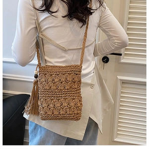 Detail view of handmade straw crossbody bag with long tassels and woven strap on model