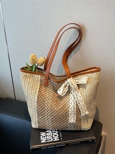 Grand sac cabas en paille tissée avec poignées en cuir et nœud en dentelle sur canapé noir