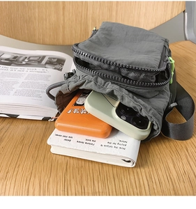 Detail view of the gray nylon crossbody bag interior holding a phone and power bank