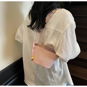 Detail of pink croc-embossed crossbody bag with gold heart pendant and logo branding
