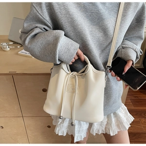 Close-up of cream bucket bag with decorative bow tag and silver metal ball drawstring detail