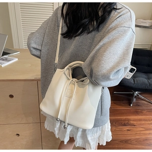 Detail of cream leather handbag featuring drawstring bow and metallic bead accents