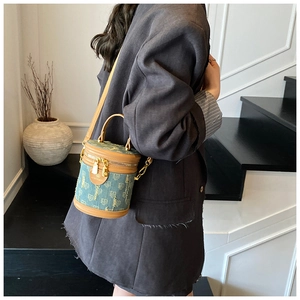 Detailed close-up of blue denim bucket bag with brown leather accents and gold hardware