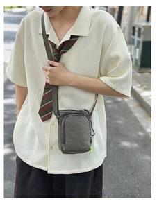 Gray nylon crossbody bag featuring two zipper compartments and green drawstring detail