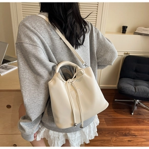 Detail of cream drawstring bucket bag with silver metal accents and crossbody strap