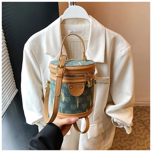 Close-up of blue jacquard denim bucket bag with brown leather handles on a blazer background