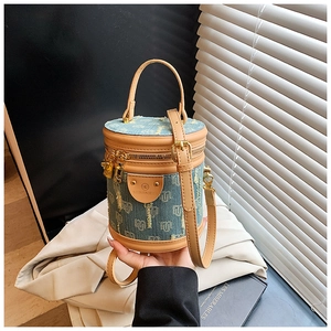 Detail of blue denim bucket bag with brown leather trim and golden zipper closure