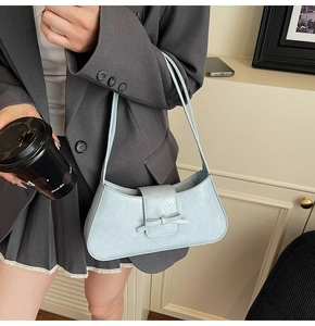 Detail view of a light blue underarm bag featuring a delicate bow and crinkled texture
