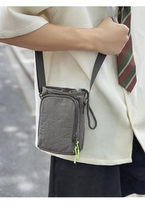Detail of grey nylon crossbody bag with drawstring closure and green paracord zipper pull