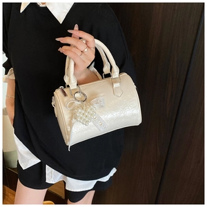 Détail du sac à main en cuir verni blanc crème avec breloque cœur perlé et nœud en dentelle