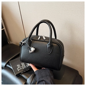 Detailed view of black pebbled leather handbag with silver whale charm and dual zippers