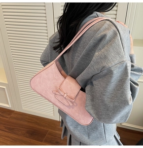 Detail of pink shoulder bag with bow magnetic clasp and ruched leather texture on model