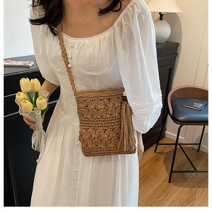 Detail of handmade straw crossbody bag with floral texture and tassel on a white dress