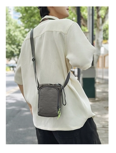 Detail of dark grey crinkle nylon crossbody phone bag with neon green zipper pullers