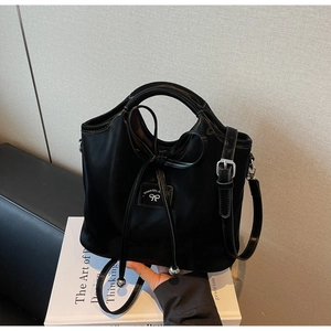 Detail of a black glossy handbag featuring a decorative bow and silver sphere charms